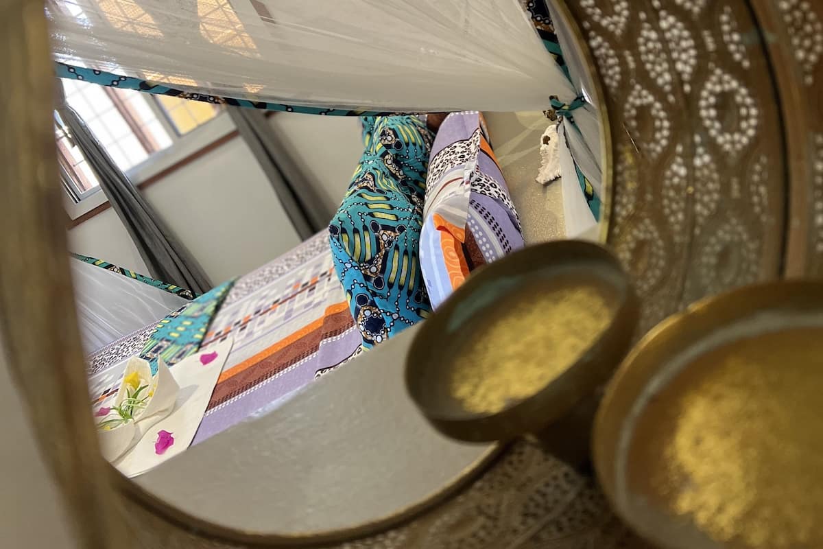 A room with a decorative mirror reflecting a patterned ceiling and a bed with colorful bedding.