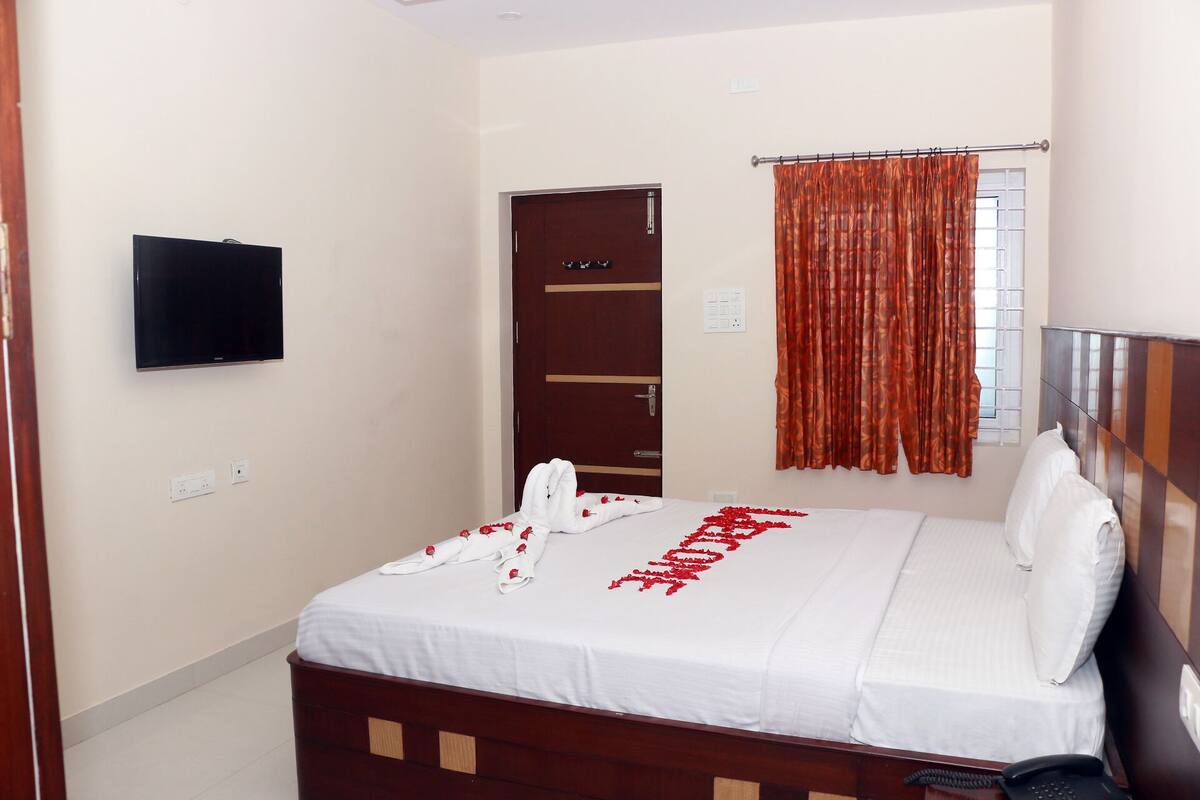 Una habitación de hotel con cama, televisión montada en la pared, una puerta y una ventana con cortinas.