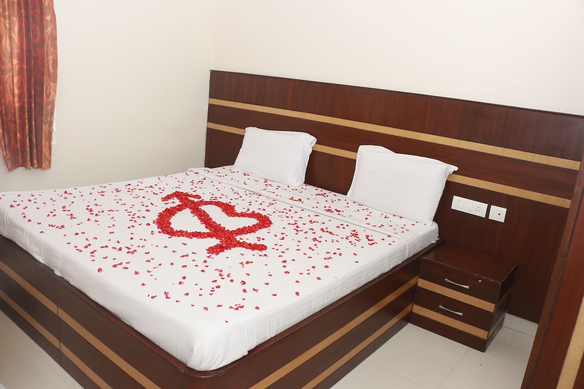 Una cama bien hecha con sábanas blancas y una decoración en forma de corazón hecha de pétalos de rosa.