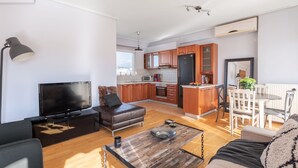 A modern apartment with a living room, kitchen, and dining area. It includes a flat-screen TV, leather sofa, wooden coffee table, and a dining table with chairs. - Penthouse w Acropolis View & Parking (Athens)