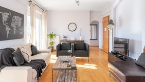 A modern living room with a sofa, a coffee table, a TV, and a clock on the wall. - Penthouse w Acropolis View & Parking (Athens)