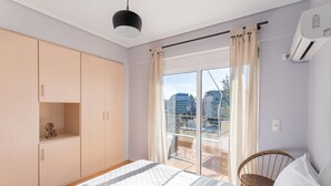 A bedroom with a bed, a wardrobe, a chair, and a balcony with a view of buildings. - Penthouse w Acropolis View & Parking (Athens)