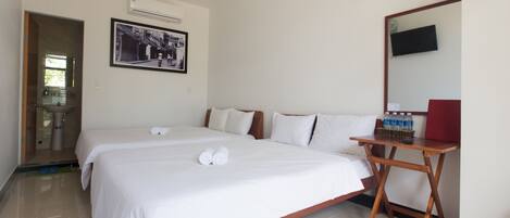 A hotel room with two beds, a wooden table, a TV, and a framed photo on the wall.