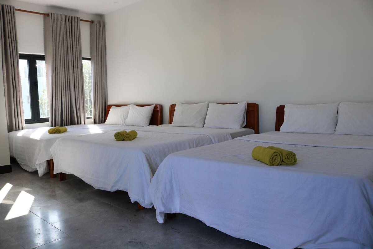 Ein Hotelzimmer mit drei Einzelbetten, alle mit weißer Bettwäsche und einem aufgerollten Handtuch.