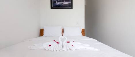 Quarto de hotel com cama bem arrumada, roupa de cama branca e um quadro na parede.