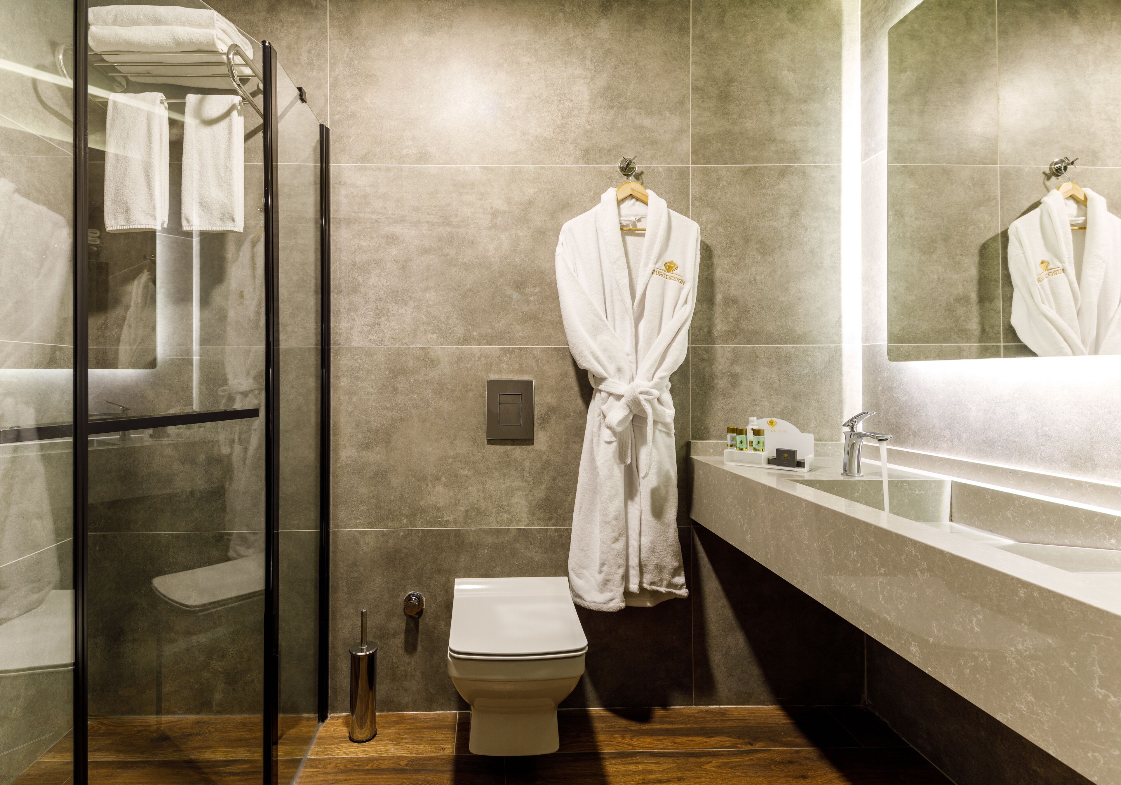 A modern bathroom with a glass shower enclosure, a toilet, a sink with a mirror, and a robe hanging on a rack.