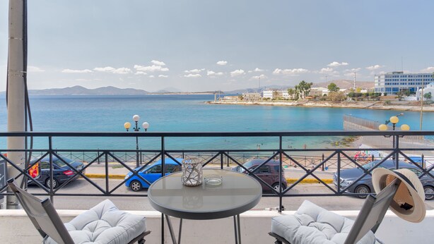 Uma varanda com vista para o mar, uma mesa com um copo e duas cadeiras.