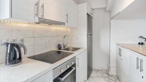Uma cozinha moderna com armários brancos, uma geladeira de aço inoxidável, uma pia dupla e uma chaleira.