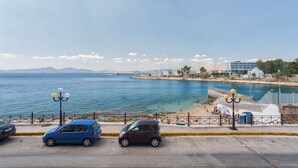 Uma estrada costeira com carros estacionados, uma praia e céu claro.