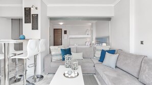 Uma sala de estar moderna com um sofá branco, uma mesa de centro e uma área de jantar com banquetas.