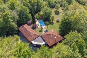 An aerial view of a property with a swimming pool, two buildings with red roofs, and surrounding greenery.