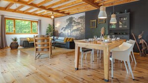 Een ruime kamer met houten vloeren, een eettafel, stoelen, een bank en een groot raam.