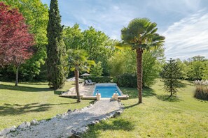 A swimming pool surrounded by greenery, with a stone pathway leading to it.
