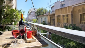A balcony with a wooden table, a bottle of wine, and two glasses. - Your home under  Acropolis Central& safe (Athens)