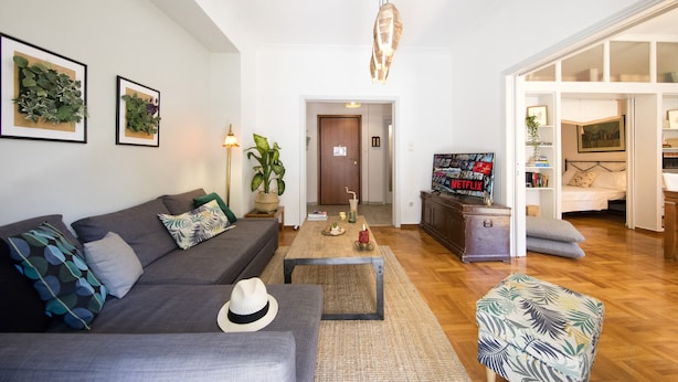 A living room with a sofa, coffee table, and a television displaying 'NETFLIX'. - Your home under  Acropolis Central& safe (Athens)