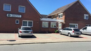 A brick building with a sign that reads "PENSION" and the number "29". There are two cars parked in front. - Pension am Meer (Norden)