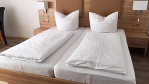 A double bed with a wooden headboard, two bedside tables with lamps, and a wooden floor. - Pension am Meer (Norden)