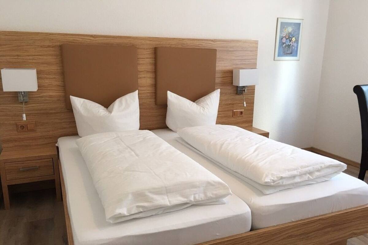A double bed with a wooden headboard, two bedside tables with lamps, and a painting on the wall.