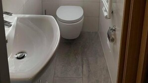 A small, modern bathroom with a white sink, toilet, and window with curtains. - Pension am Meer (Norden)