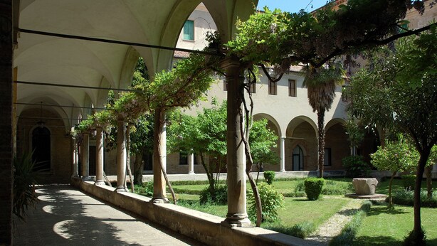 Un patio con arcos, columnas y abundante vegetación.