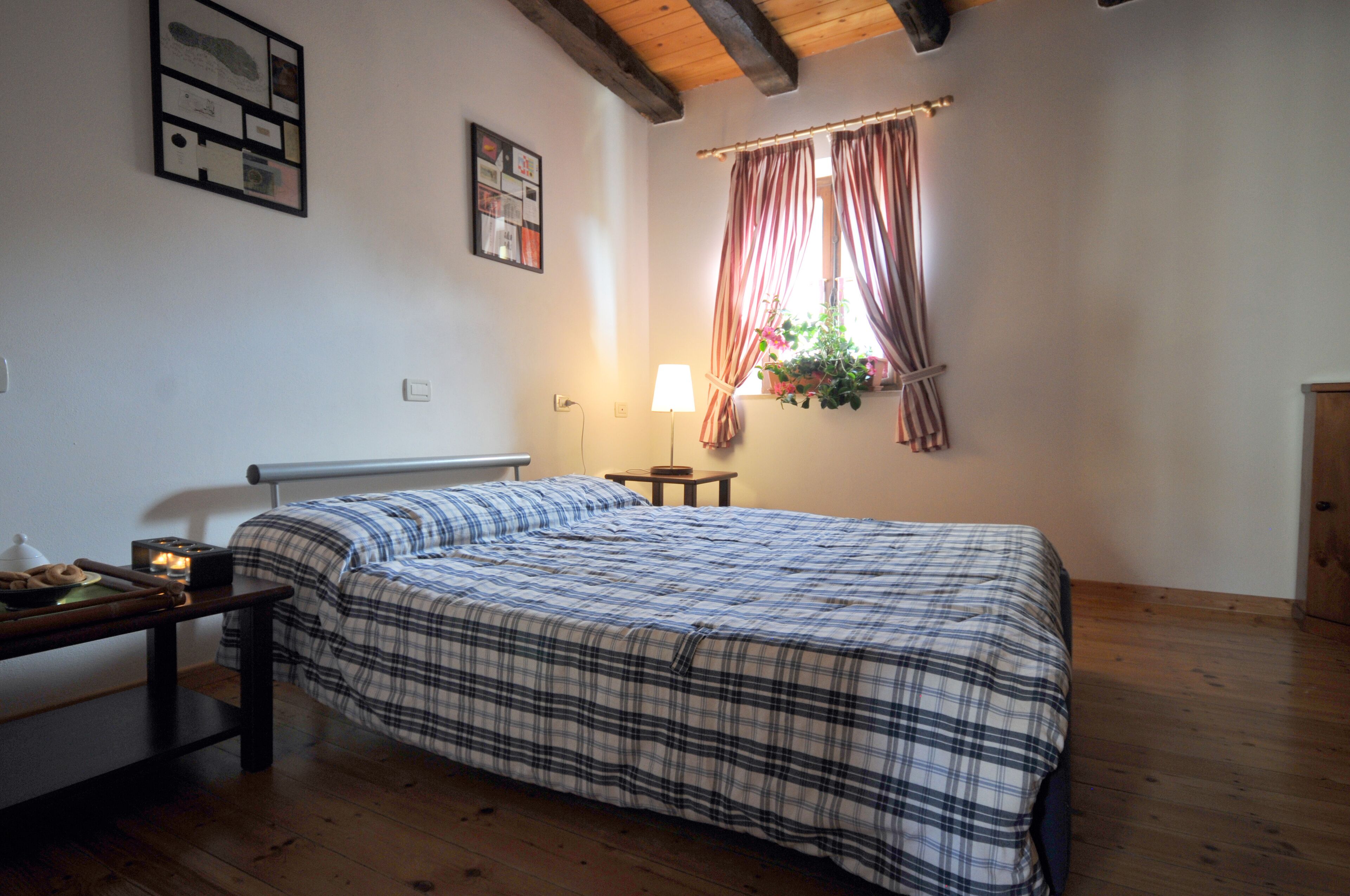 Un dormitorio con cama, mesita de noche, lámpara y ventana con cortinas.