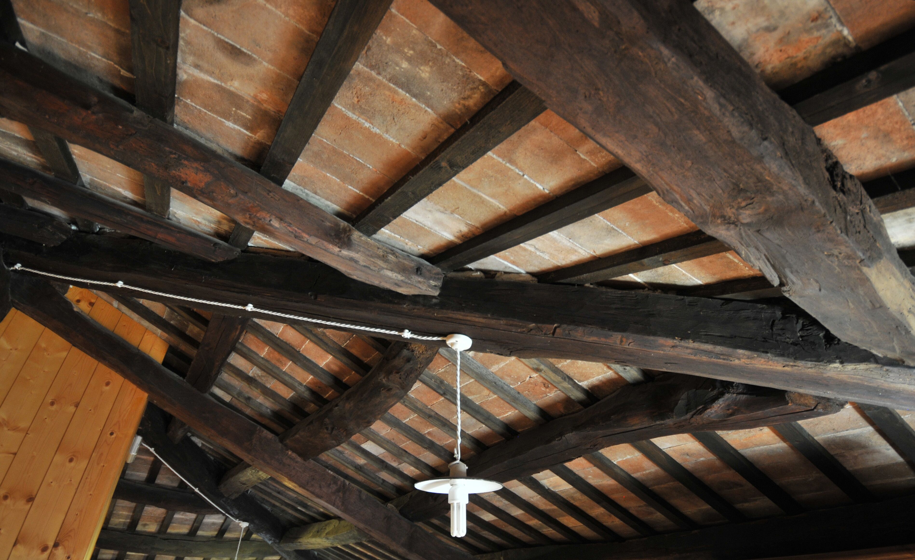 Un plafond en bois avec des poutres apparentes et un luminaire suspendu.