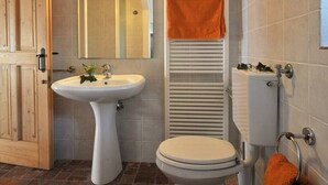 Un baño con lavamanos pedestal, inodoro y un perchero con una toalla naranja.