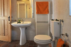 Une salle de bain avec un lavabo sur colonne, des toilettes et un porte-serviettes sur lequel est posée une serviette orange.