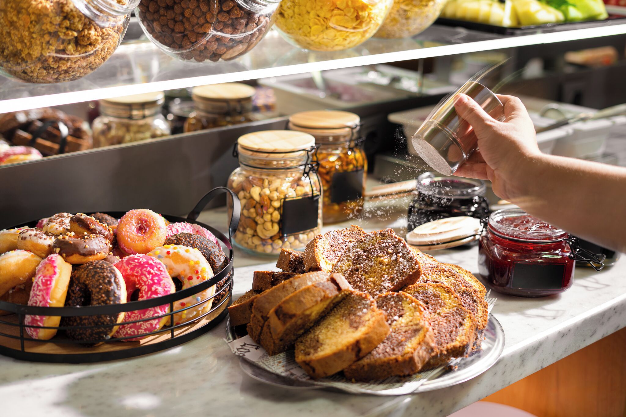 Variedad de productos horneados expuestos en una barra, incluyendo rosquillas, pan y pastelería.