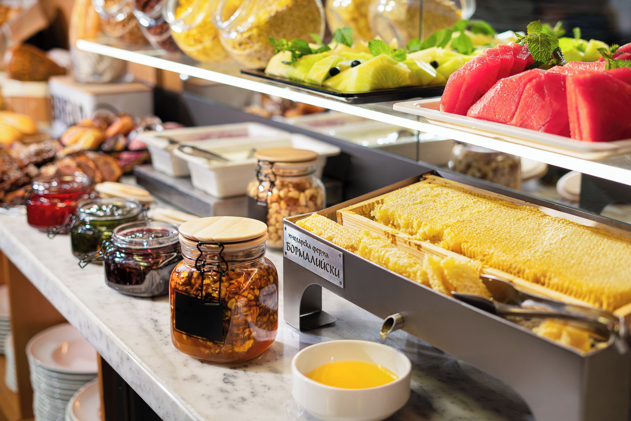 A buffet with various food items including honeycomb, fruits, and jams.