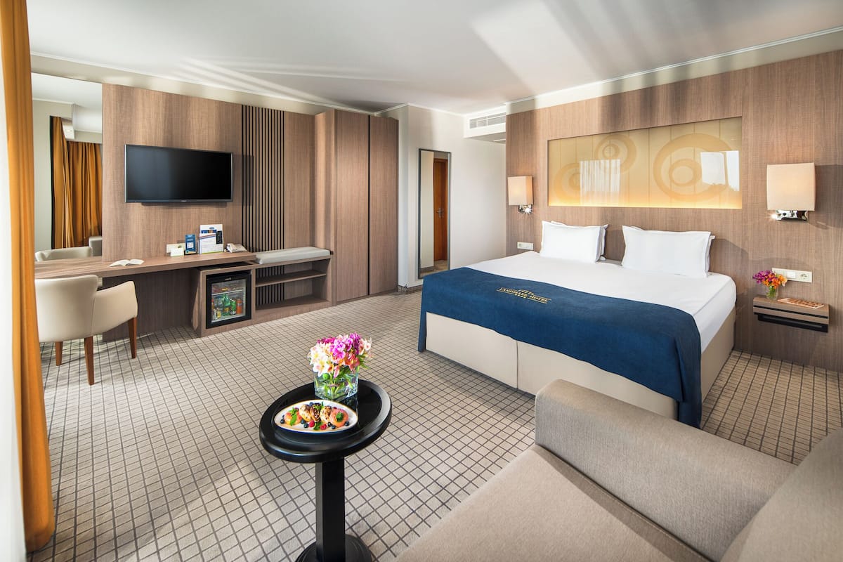 A hotel room with a bed, a desk, a TV, a small table with flowers, and a sofa.