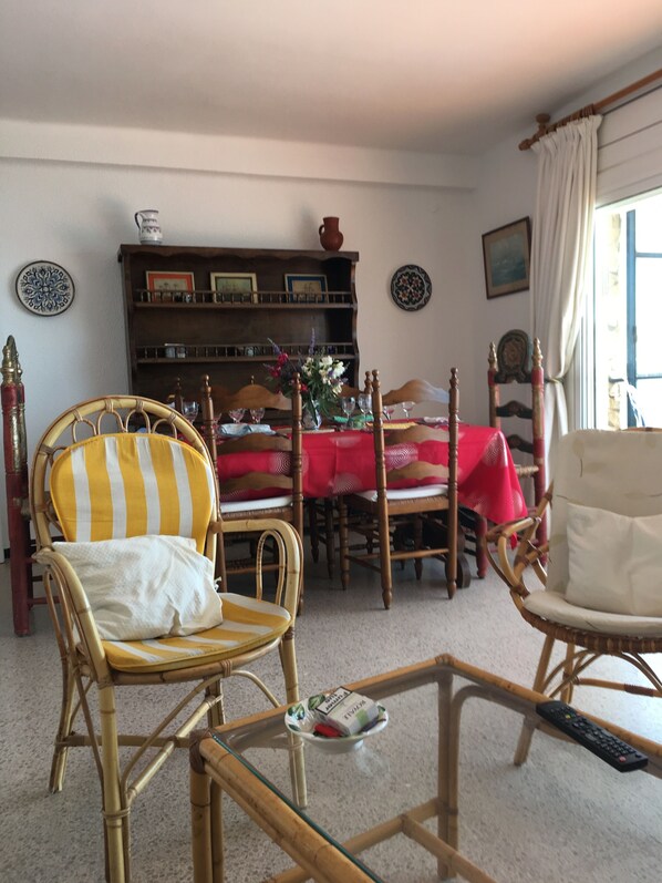 A living room with a dining table, two chairs, a bookshelf, and a window with curtains.