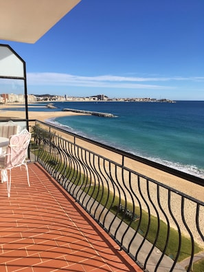 A balcony with a view of the beach and ocean, featuring a table and chairs.