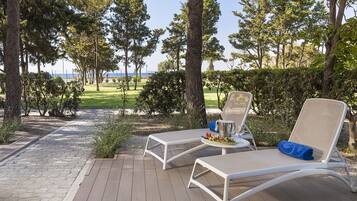 Una terraza con dos sillones blancos, una mesita con bebidas y aperitivos, y vista al mar entre los árboles.