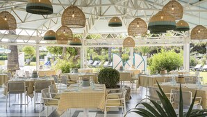 An outdoor dining area with tables and chairs, covered by a white roof, and hanging wicker lamps. - The Signature Level at Grand Palladium Sicilia Resort & Spa (Campofelice di Roccella)