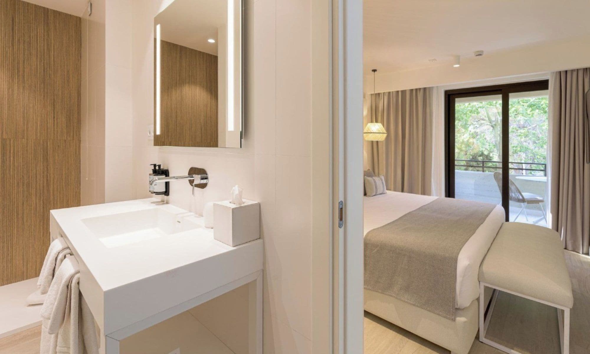 Una habitación de hotel moderna con un amplio tocador de baño, un dormitorio independiente con balcón y un espejo grande.