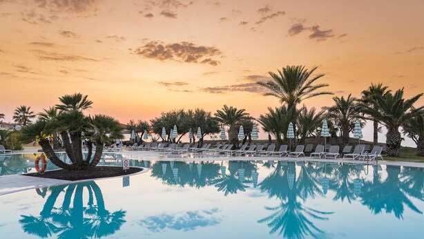A poolside area with lounge chairs and palm trees, reflecting the sunset sky. - The Signature Level at Grand Palladium Sicilia Resort & Spa (Campofelice di Roccella)