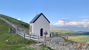 A small white church with a cross on top, surrounded by a stone wall and wooden fence, set against a backdrop of a mountainous landscape. - Apartment HaNiLe with "honeymoon suite" with dream view - max. 14 pers (Sarnthein)