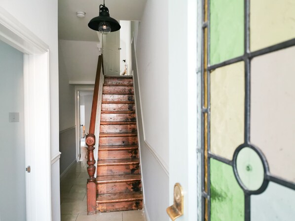 A wooden staircase with a black pendant light, leading to a room with a green and yellow stained glass door.