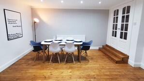 A dining area with a table set for four, surrounded by chairs, a floor lamp, and a framed quote on the wall. - Railway Street by Switchback Stays (Cardiff)
