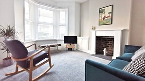 A living room with a sofa, a rocking chair, a television, a fireplace, and large windows. - Railway Street by Switchback Stays (Cardiff)