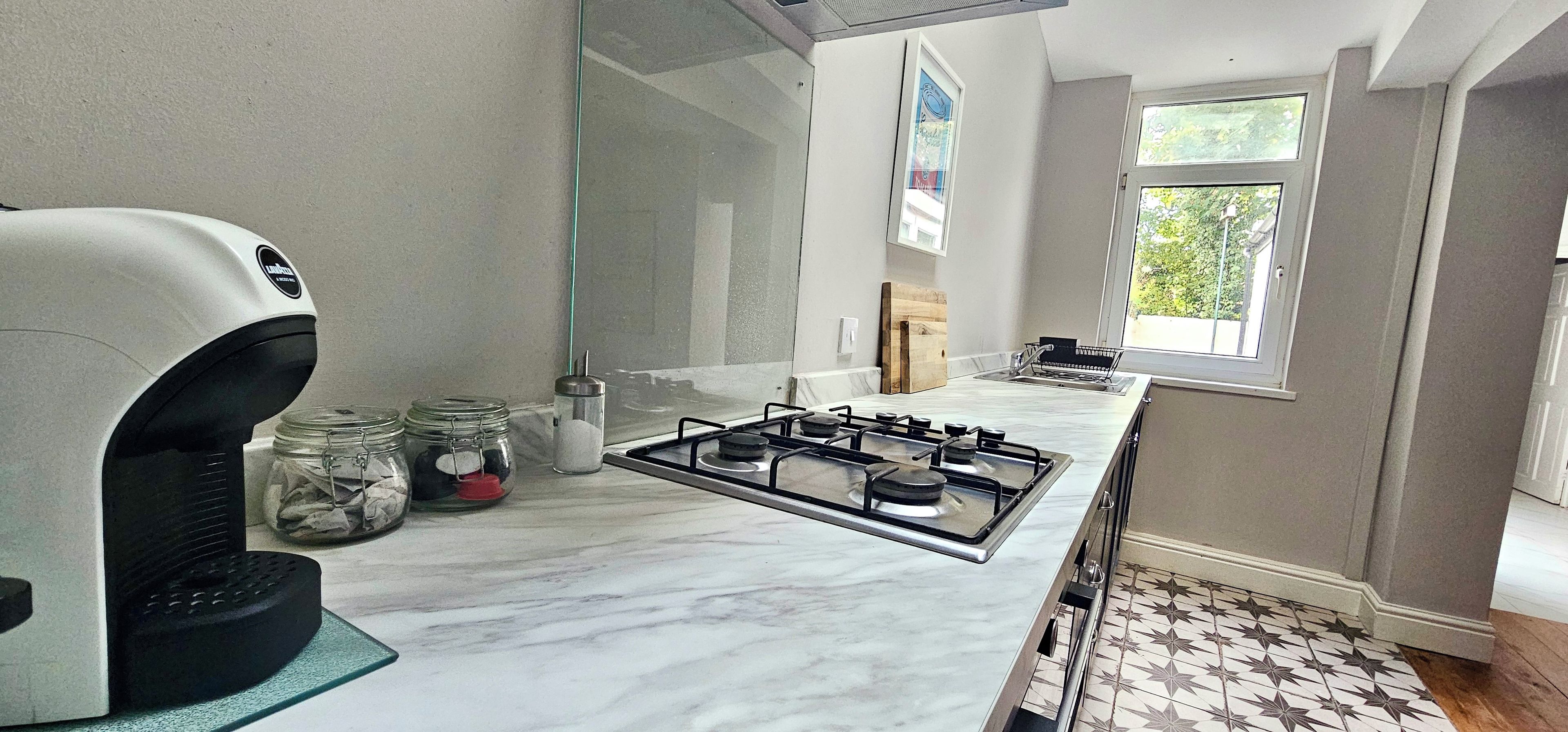 A kitchen with a gas stove, a coffee maker, and jars on the counter.
