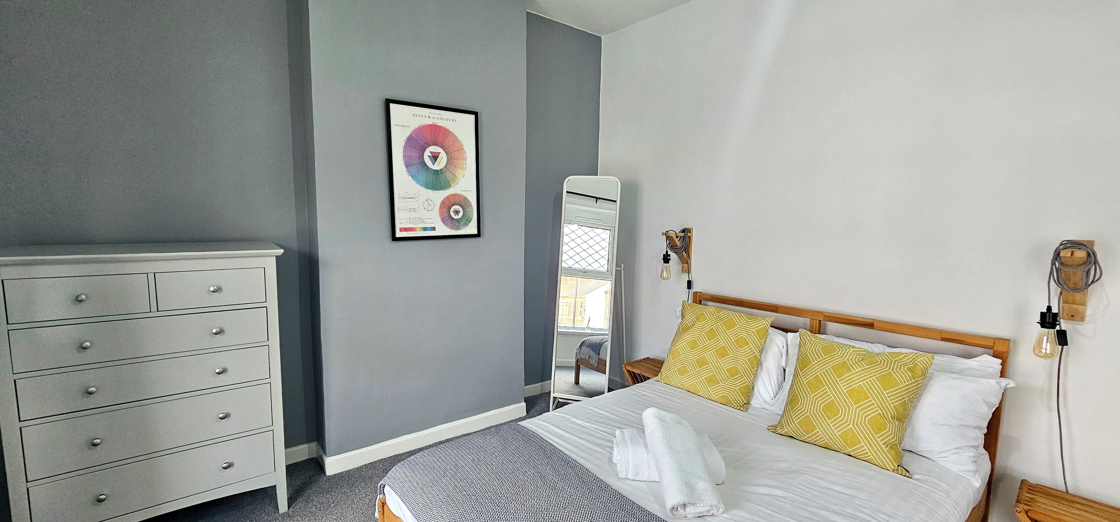 A bedroom with a bed, a dresser, a mirror, and a wall-mounted light fixture.