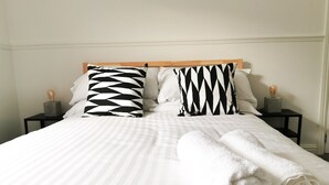 A neatly made bed with striped bedding, two black and white patterned pillows, and a rolled white towel on the side. - Railway Street by Switchback Stays (Cardiff)