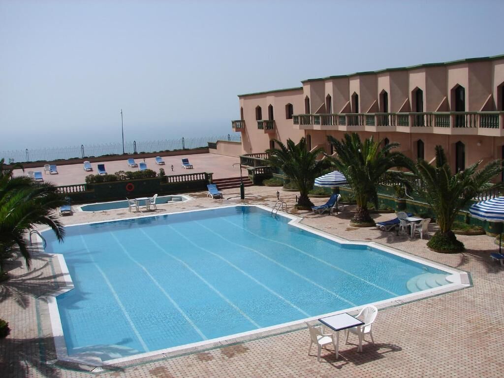 Ein großer Pool mit Liegestühlen und Sonnenschirmen, umgeben von einem Gebäude mit einem Balkon.