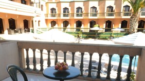 A balcony with two chairs and a table, a bowl of fruit, and a view of a building with balconies and a palm tree. - Atlantique Panorama (Safi)