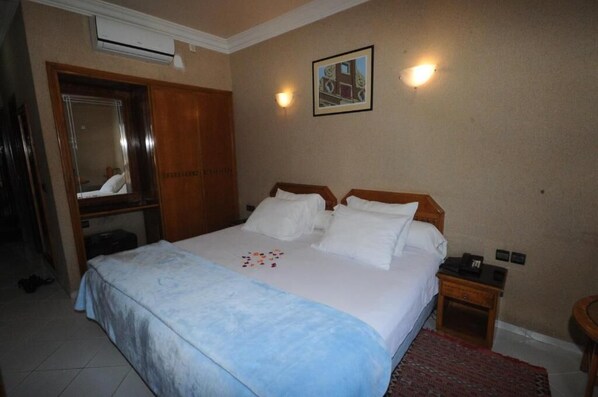 A hotel room with a large bed, a wooden wardrobe, a bedside table, and a small round table.