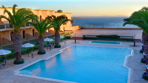 A pool area with palm trees, lounge chairs, and a view of the sea. - Atlantique Panorama (Safi)