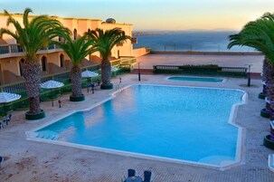 Una piscina al aire libre, sombrillas, sillones reclinables de piscina
