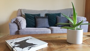 Una sala de estar con un sofá gris, una mesa de centro blanca y una planta en maceta.